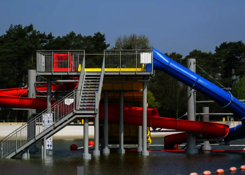 Ein Rutschenturm mit drei Wasserrutschen führt in ein flaches Becken im Freien.