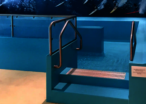 Run-outs of a water slide with water collection basin and stainless steel railing in front of a surfer wall motif.