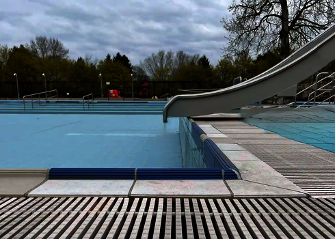 Die Kastenrutsche mündet seitlich ins flache Wasser eines Kinderbeckens im Freibad.