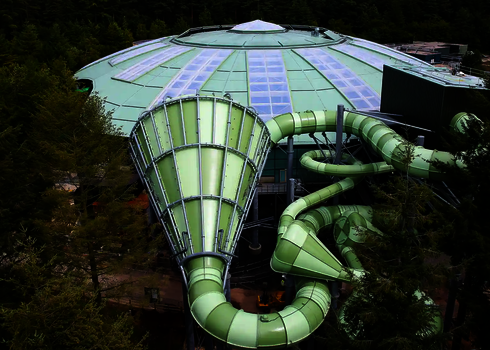 Gesamtansicht des Cyclone-Trichters mit Röhrenrutschen, eingebettet in bewaldeter Umgebung.