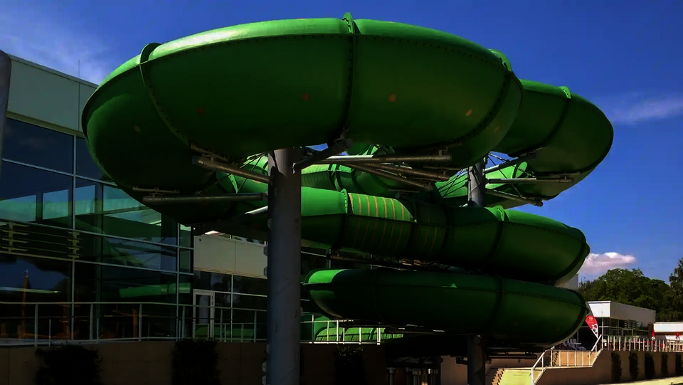 Grüne Family Twister Rutsche vor dem modernen Schwimmbadgebäude.