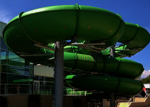 Grüne Family Twister Rutsche vor dem modernen Schwimmbadgebäude.