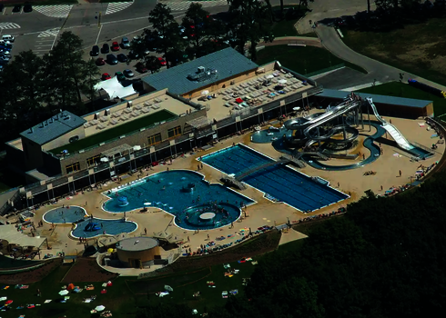 Vogelperspektive auf eine Wasserpark mit mehreren Schwimmbecken, Wasserrutschen und Liegewiesen.