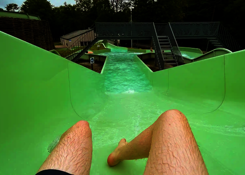 Eine Person rutscht einen grünen Wildwasserfluss, im Hintergrund Treppen.