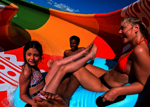 Drei Personen rutschen auf einem großen Reifen durch eine bunte Family Twister Wasserrutsche.