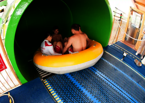 Vier Personen sitzen im Rutschreifen und starten gemeinsam eine Fahrt durch die grüne Rutsche.