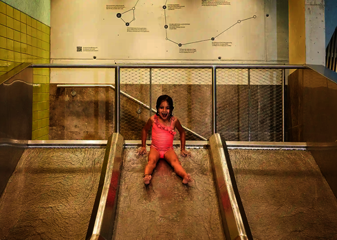 Ein Mädchen sitzt lachend auf der mittleren Bahn der Trio-Slide im Kinderbereich.