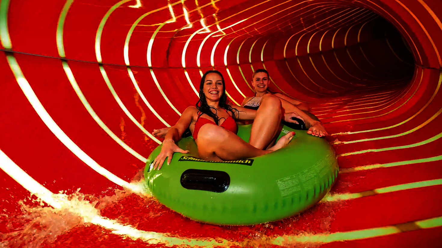 Zwei Frauen fahren auf grünem Reifen durch rot beleuchteten Family Twister.