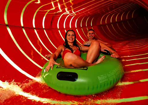 Zwei Frauen fahren auf grünem Reifen durch rot beleuchteten Family Twister.
