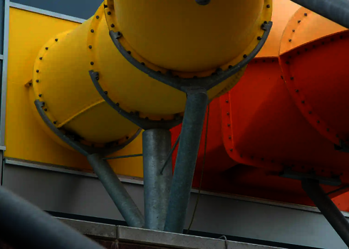 Gelbe und orange Wasserrutschen verlassen nebeneinander das Gebäude.