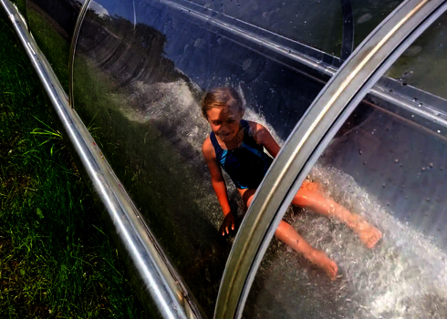 Ein Mädchen rutscht durch den gläsernen Tunnel einer WR1040 Rutsche im Grünen.