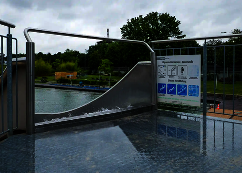 Startbereich einer Edelstahl Wasserrutsche mit Hinweistafel und Sicherheitsstange.