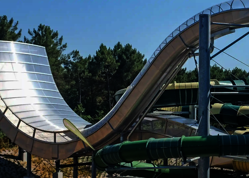 Outdoor-Boomeang-Rutsche aus Edelstahl mit Kurvenrutsche im Hintergrund und Waldkulisse.