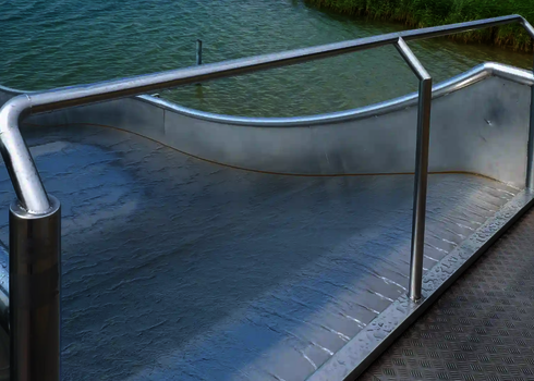 Startbereich einer Breitwellenrutsche mit einer Sicherheitsstange, im Hintergrund ein See.