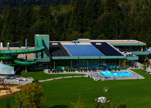 Außenansicht eines Schwimmbads mit grüner Family Twister Wasserrutsche und Liegewiese.