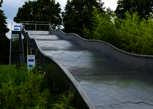 Eine Breitwellenrutsche mit Hinweisschildern, im Hintergrund Pflanzen und Bäume.