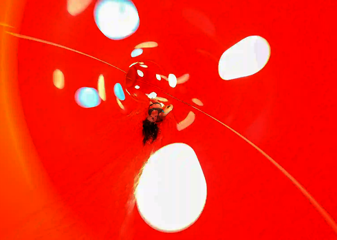 Eine rote Wasserrutsche von innen mit gepunkteten Tageslichteffekten und einer rutschenden Frau.