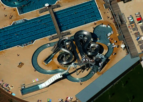 Vogelperspektive auf einen Wasserpark mit einem Edelstahl-Rutschenkomplex und mehreren Schwimmbecken.