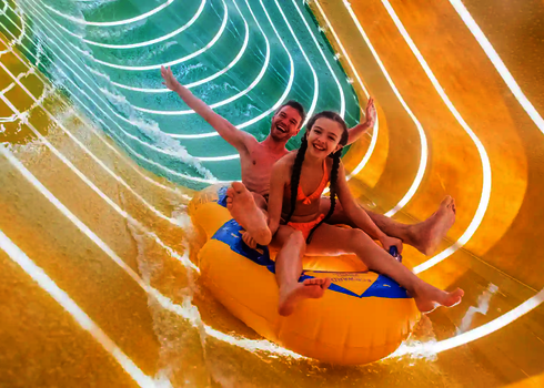Ein Mann und ein Mädchen genießen die Fahrt im gelb-blauen Reifen durch die gelb leuchtende Family Twister.