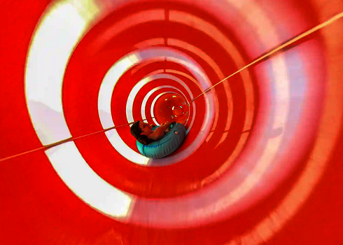 Person rutscht im Reifen durch eine Röhrenrutsche mit gestreiften Lichtspiel-Effekten.