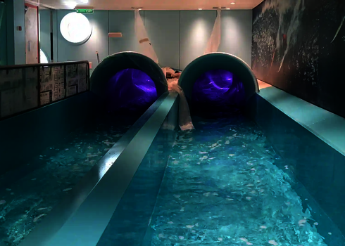 Two purple tube slides end in a turquoise indoor splash pool.