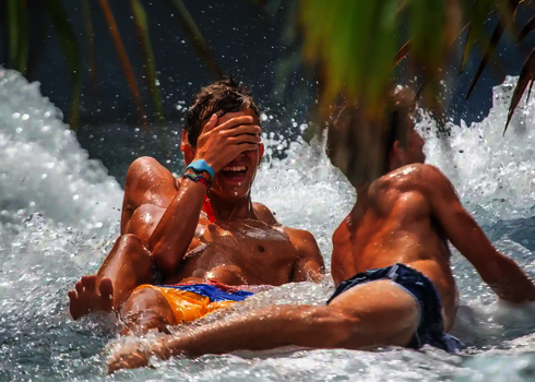 Zwei Jungen rutschen lachend nebeneinander durch den Wildwasserfluss.
