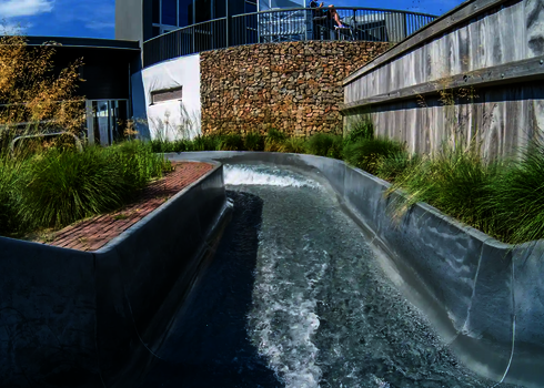 Gerade Strecke des Wildwasserflusses mit leichtem Gefälle, eingerahmt von Gras und Holzverkleidung.
