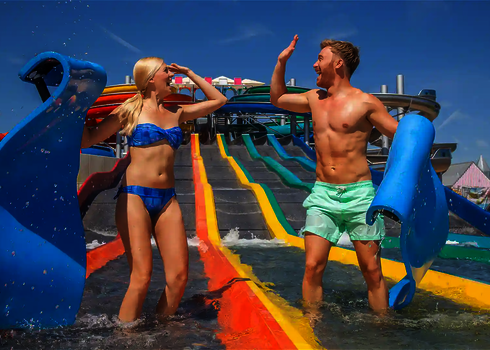 Two young adults celebrate at the end of the matracer water slide with slide mats in the outdoor pool.