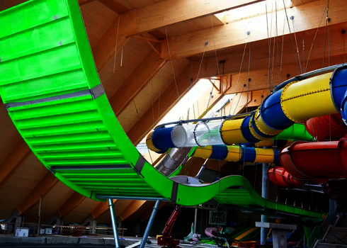 Grüne Boomerang-Rutsche im Bau und umliegenden bunten Röhrenrutschen.