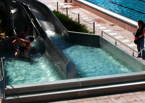Two stainless steel slides end side by side in a catch basin, where children climb out.
