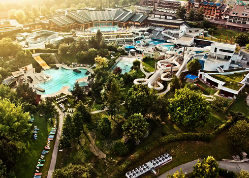 Außenaufnahme eines Wasserparks mit mehreren Pools und der Raft Racer Reifenrutsche im Grünen.