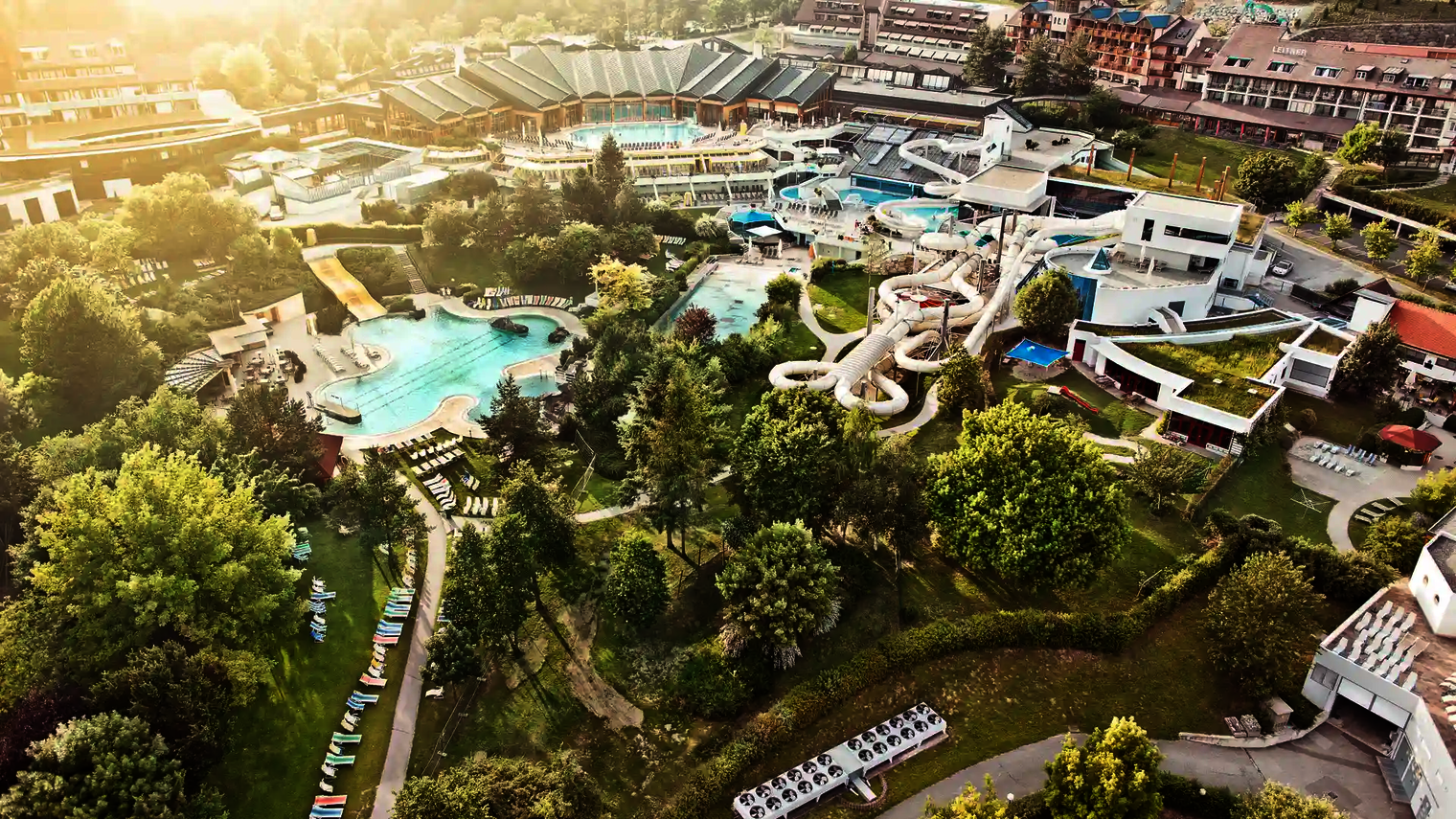 Außenaufnahme eines Wasserparks mit mehreren Pools und der Raft Racer Reifenrutsche im Grünen.
