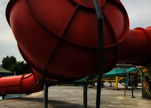 Ein roter Crazy Cone endet in einem flachen Wasserbecken, im Hintergrund ein Pavillondach