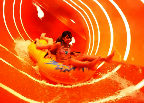 Mädchen rutscht auf gelbem Reifen durch die orangene Family Twister Wasserrutsche mit Lichtstreifen.