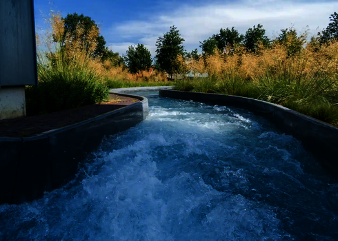 Sprudelndes Wasser fließt durch den Wildwasserfluss, eingerahmt von Gräsern und Bäumen.