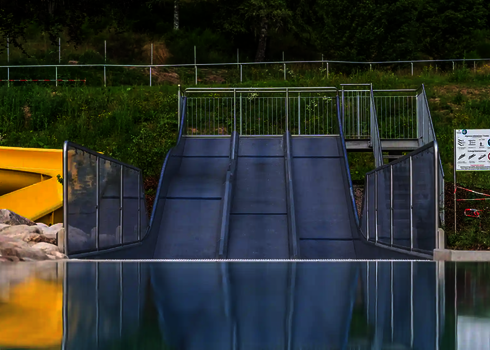 Trio-Slide im Freien mit Blick auf gelbe Spiralrutsche und bewaldete Umgebung.