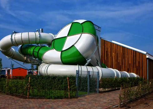 Body Cone Wasserrutsche in Grün und Weiß neben moderner Holzfassade und braunen Gebäude