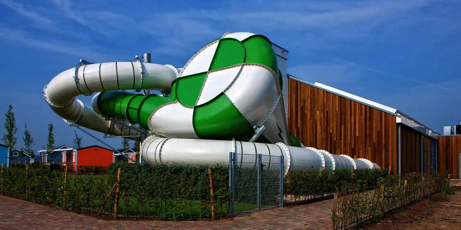 Body Cone Wasserrutsche in Grün und Weiß neben moderner Holzfassade und braunen Gebäude