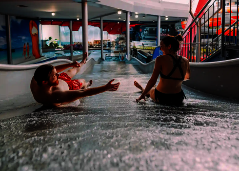 Zwei Personen rutschen lachend eine Breitwellenrutsche hinunter.