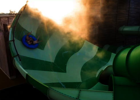 Mehrere Personen auf Rutschreifen fahren durch die dampfende Lotus Wasserrutsche.