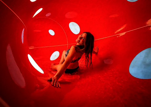 Frau rutscht in einer roten Röhrenrutsche mit gepunkteten Lichtspiel-Effekten.