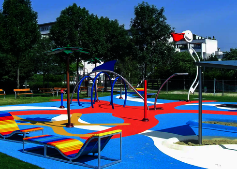 Moderner, bunter Wasserspielplatz mit unterschiedlichen Wie-Spray Elementen in parkähnlicher Umgebung.