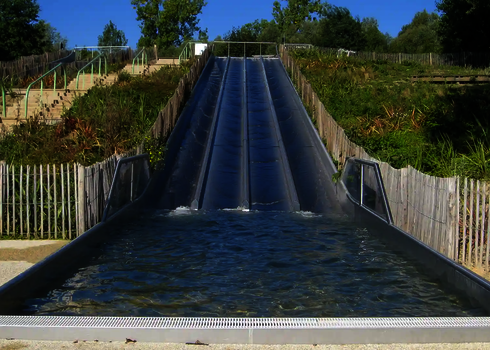Eine Breitwellenrutsche aus Edelstahl, die einen grün bewachsenen Hang hinabgeht.