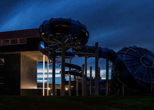 Blauer Cyclone bei Abenddämmerung mit beleuchteter Röhrenrutsche und modernem Startturm.