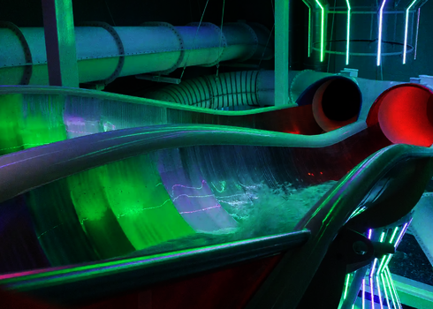 Startbereich der Raft Racer Reifenrutsche mit grün-pinker Beleuchtung und leeren Röhren.