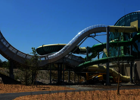 Grüne und gelbe Wasserrutschen verlaufen aus einem verglasten Gebäude ins Freie.