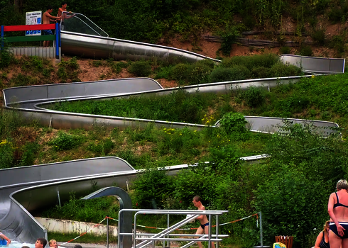 Lange Edelstahl-Wasserrutsche WR1040 mit mehreren Kurven an einem Hang in einem Freibad.