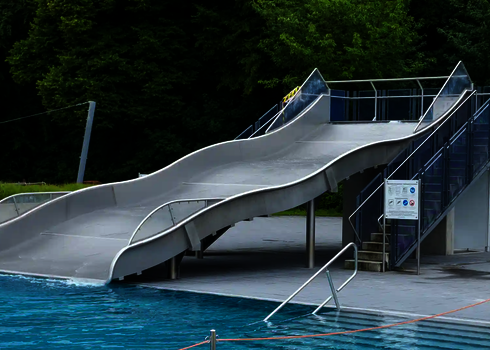 Eine Breitwellenrutsche aus Edelstahl in einem Schwimmbad, die in ein Schwimmbecken übergeht.