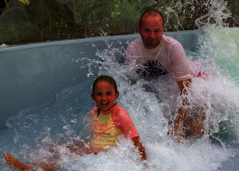 Ein Mädchen und ein Mann landen lachend gemeinsam im Wildwasserbecken.