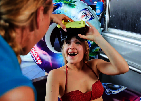 Eine Frau in Badebekleidung setzt sich lachend eine gelbe VR-Brille auf.